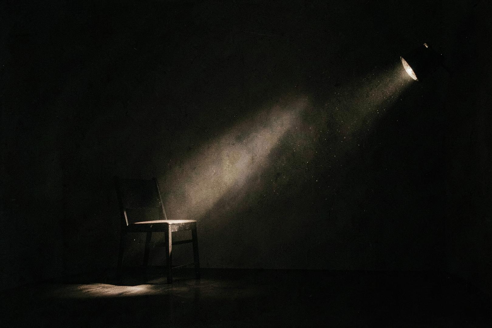 A single chair lit by a projector beam in a dark room